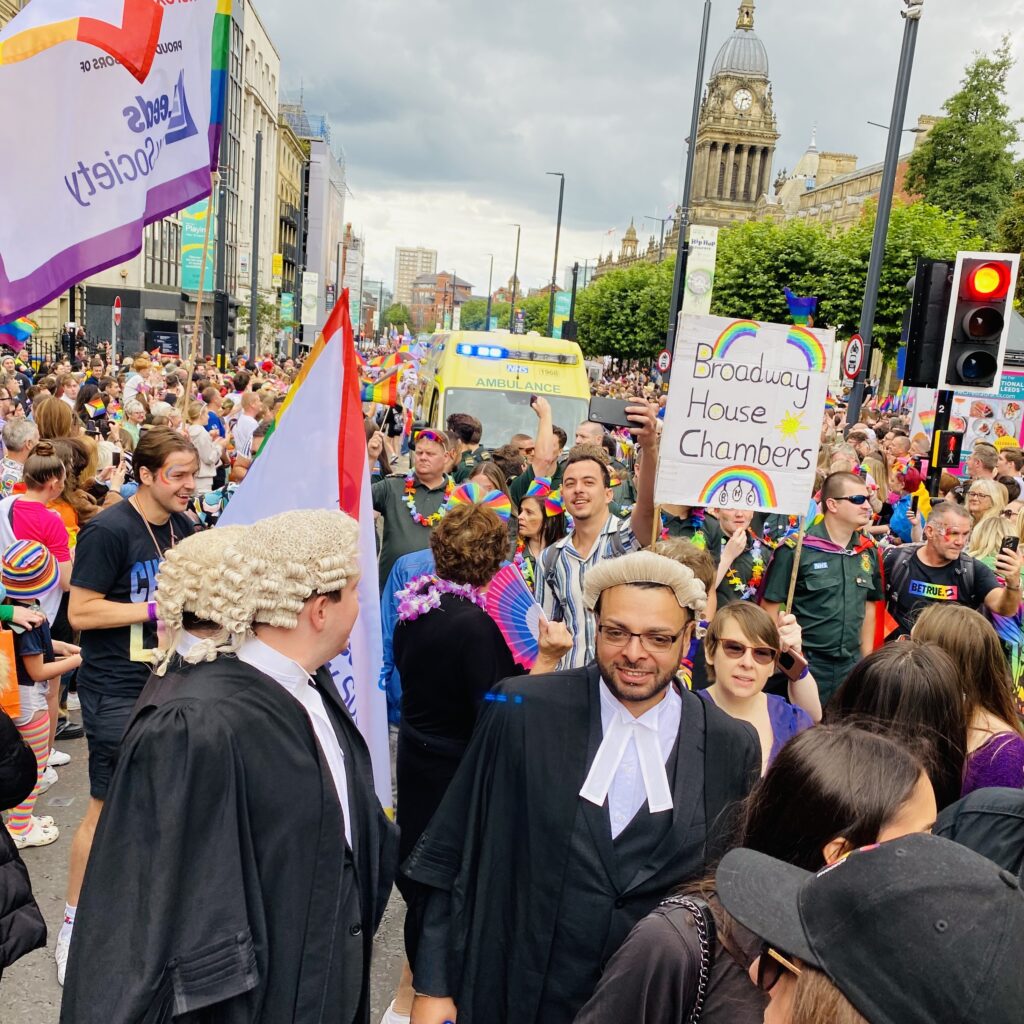 Image show a large crowd of people with barristers in the foreground wearing wigs and robes